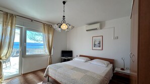 A bedroom with a bed, a TV, and a view of the sea through a sliding door. - Azure Apartments By The Sea with 3 Bedrooms (Omis)