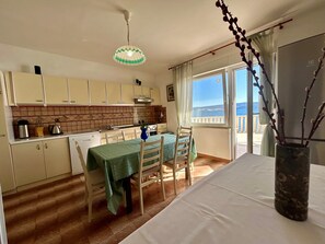 Een kleine keuken met een eethoek, uitzicht op zee en een balkon met een hekwerk.