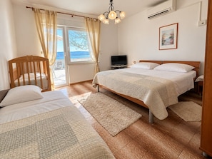 A bedroom with two beds, a television, a window with curtains, and a painting on the wall.