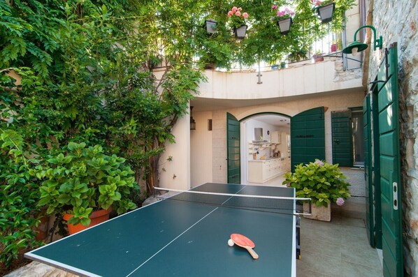 A courtyard with a ping pong table, green doors, and a kitchen visible through an archway.