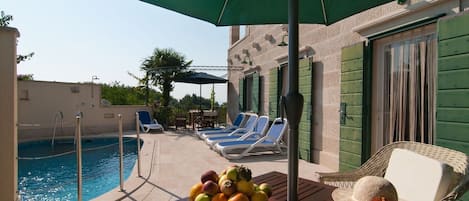 A poolside area with lounge chairs, a table with fruit, and a covered umbrella.