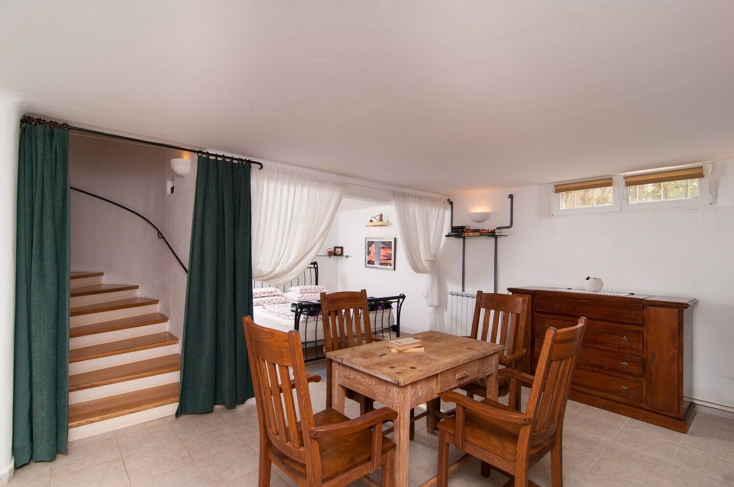 A dining area with a wooden table and chairs, a staircase with green curtains, and a radiator.