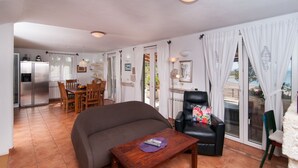 A cozy living area with a sofa, a coffee table, and a dining table with chairs. There is a black leather chair with a floral cushion and a view of the sea through large windows. - NEW! Exclusive Beachfront Villa with Pool for 8 at Island Brač (Mirca)