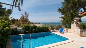 A swimming pool with a view of the sea, surrounded by greenery and a stone structure. - NEW! Exclusive Beachfront Villa with Pool for 8 at Island Brač (Mirca)
