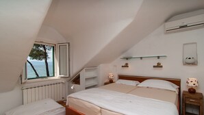 A bedroom with a large bed, a window with a view of trees and water, a radiator, a shelf, and a bedside table with a lamp. - NEW! Exclusive Beachfront Villa with Pool for 8 at Island Brač (Mirca)