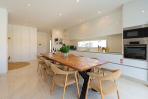 Una cocina moderna con armarios blancos, una mesa de comedor de madera con sillas y un horno empotrado.