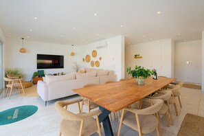 Una sala de estar moderna con una mesa de comedor de madera, sofás color beige y un televisor de pantalla plana montado en la pared.