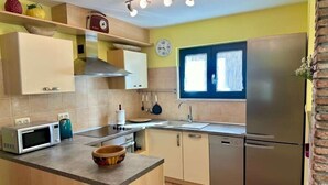 Eine kompakte Küche mit Mikrowelle, Toaster und Wasserkocher auf der Arbeitsplatte, einem Spülbecken und einem Kühlschrank.
