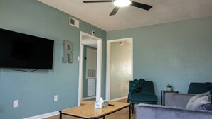 Een woonkamer met turquoise wanden, een plafondventilator, een flatscreentelevisie, een salontafel en twee banken.