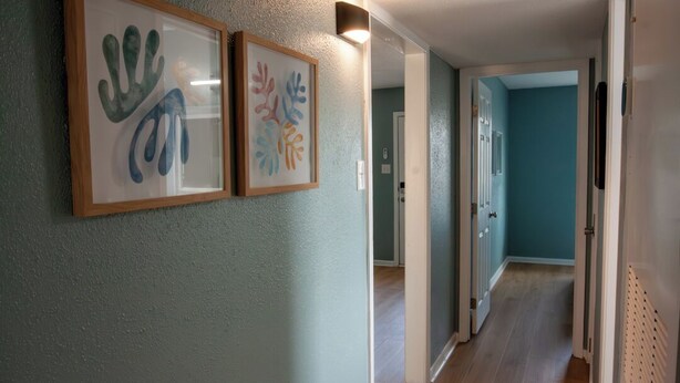 Een gang met twee kunstwerken in lijsten aan de muur, een deur naar een andere kamer en een lamp boven de deur.