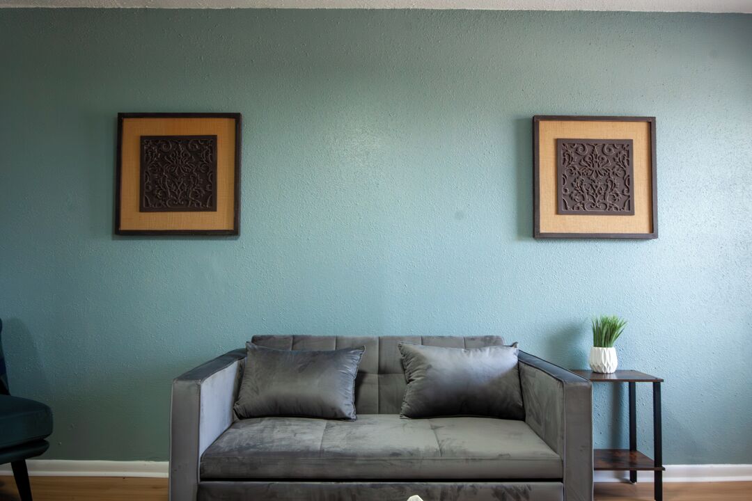 A living room with a grey sofa, two framed wall decorations, and a small side table with a plant.