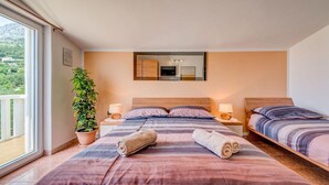 Une chambre d’hôtel avec deux lits, une grande fenêtre, une plante en pot et un miroir au mur.