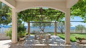 A covered outdoor seating area with stone flooring, a pergola with climbing plants, and a view of the sea. - Apartment for 4 Persons With Pool (Stanici)