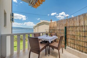 Een balkon met rieten meubels, een tafel met een fles en fruit, en uitzicht op zee.