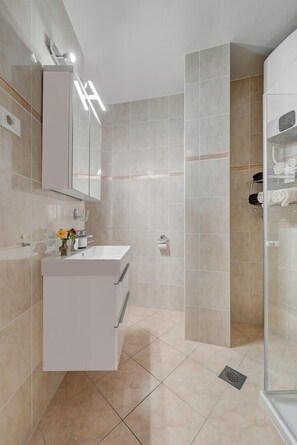Een moderne badkamer met een wit wastafelmeubel, een douchecabine met glazen wanden en beige tegels.