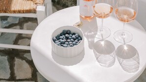Una mesa blanca con una botella de vino rosado, dos copas y un bol de arándanos.