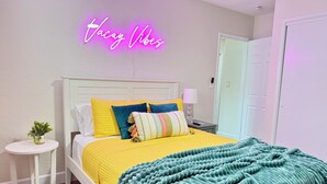 A neatly arranged bedroom with a bed, pillows, a bedside table, a lamp, and a neon sign. - HUGE GameRoom | Steps 2 Beach | Golf Simulator | Movie Theater (Daytona Beach)