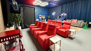 A room with a red sofa, a small white table, a basketball hoop, and a neon sign. - HUGE GameRoom | Steps 2 Beach | Golf Simulator | Movie Theater (Daytona Beach)
