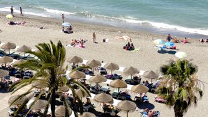 Ein Strand mit Liegestühlen, Sonnenschirmen, Palmen und dem Meer.