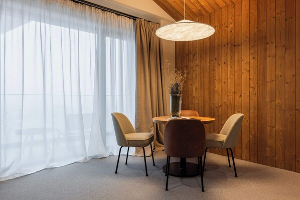 A dining area with a round table, two chairs, a vase with dried flowers, and a hanging light fixture. - The Pines Bucegi Lodge (Bran)