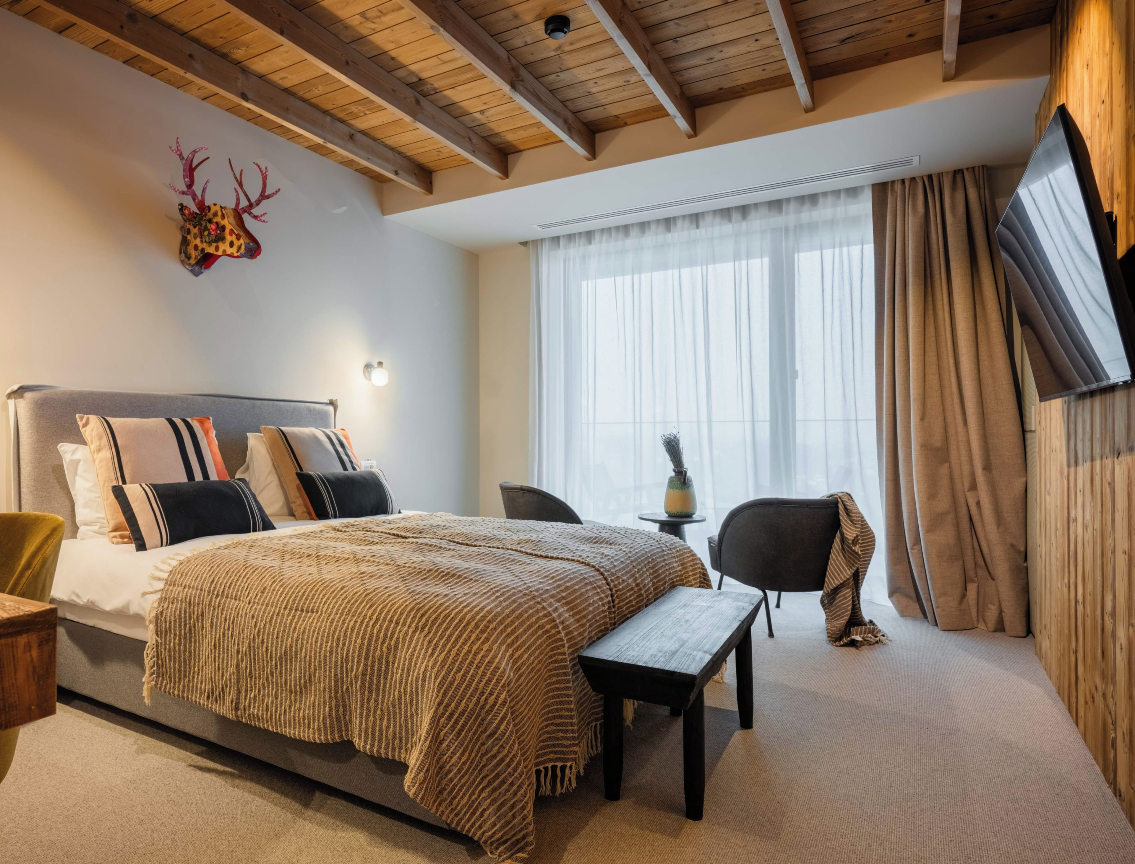 A bedroom with a bed, bedside tables, a desk, a chair, a TV, and a window with curtains.
