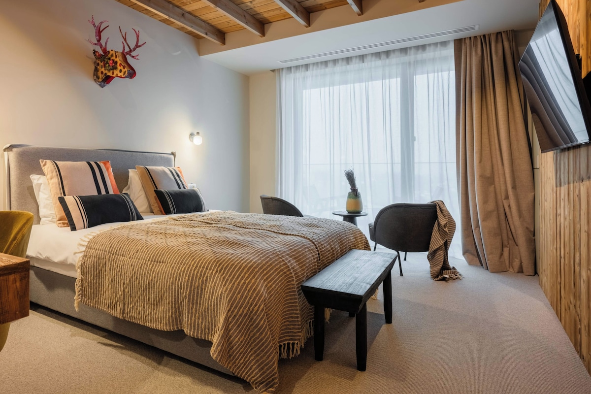 Un dormitorio con cama, mesitas de noche, un escritorio, una silla, un televisor y una ventana con cortinas.