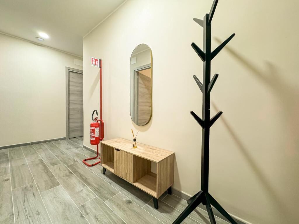 A hallway with a wooden vanity, a round mirror, a coat rack, and a fire extinguisher.
