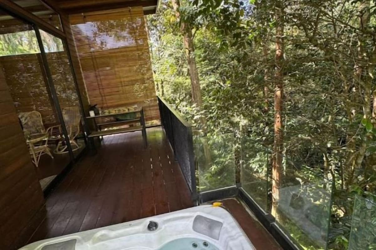 Una terraza de madera con un jacuzzi, con vistas a un área boscosa.