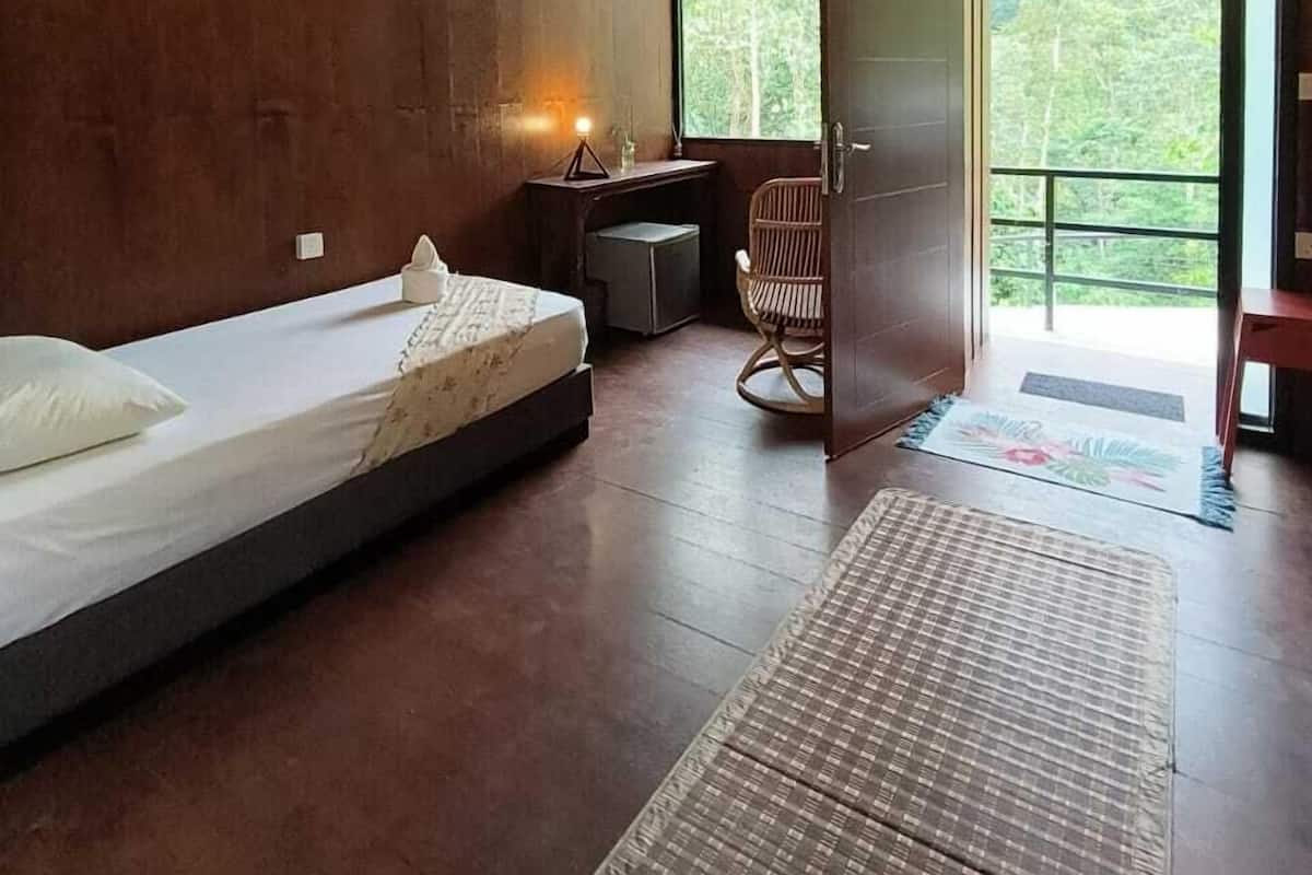 Quarto com cama, escrivaninha, cadeira e uma janela grande.