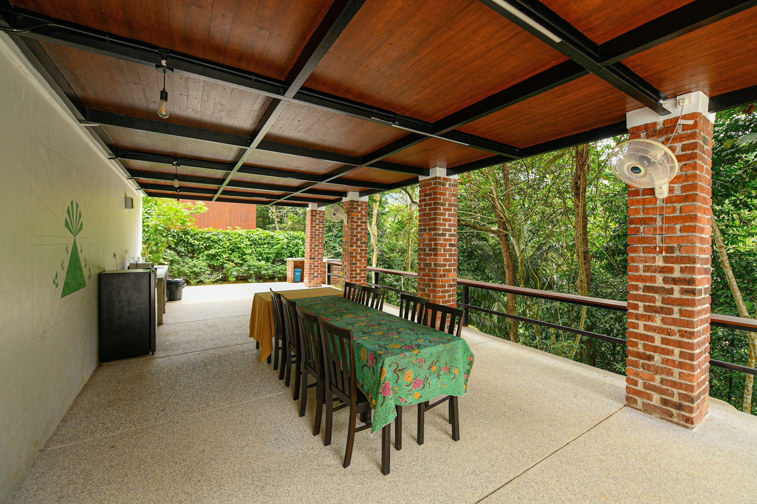 An outdoor covered patio with a long table and chairs, surrounded by brick pillars and a railing.