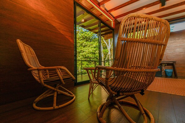 Dos sillas mecedoras de mimbre en una habitación con paredes de madera y un amplio ventanal que da a un espacio exterior.