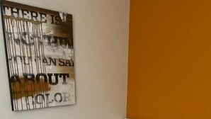 Ein Zimmer mit einem Einzelbett, einer weißen Matratze und einem Kissen, einem weißen Nachttisch und einem an der Wand hängenden Kunstwerk mit Text.