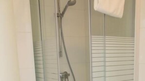 Eine gläserne Duschkabine mit Handbrause und einem Handtuch an der Wand.