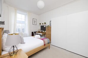 A modern bedroom with a bed, bedside table, lamp, desk, chair, and wardrobe.