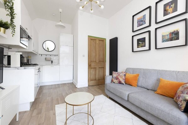 A modern kitchen with white cabinets, a round mirror, and a wooden door. - Bright and Modern Flat with desk (Edinburgh)