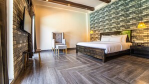 A modern bedroom with a large bed, a chair, and a TV mounted on a brick wall. - Vanya Forest Resort (Kaladhungi)
