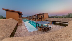 A rooftop pool area with a thatched roof, a lounge with a round table, and a view of the surrounding buildings. - Vanya Forest Resort (Kaladhungi)