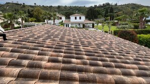 A terracotta-tiled roof with a view of a white building surrounded by greenery.