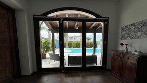 A room with a sliding glass door leading to a pool area, a tiled floor, and a cabinet with a vase and candle.