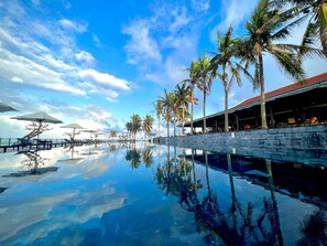 A pool with palm trees and umbrellas, reflecting the sky and clouds. - Ocean Villa Da Nang 4BR 5 Beds, Private Pool and Kitchen (Da Nang)