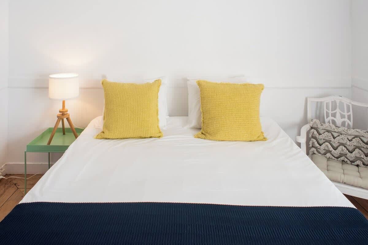 A neatly made bed with two pillows, a bedside lamp, and a chair with a patterned cushion.