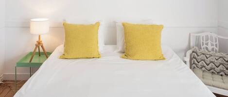 A neatly made bed with two pillows, a bedside lamp, and a chair with a patterned cushion.