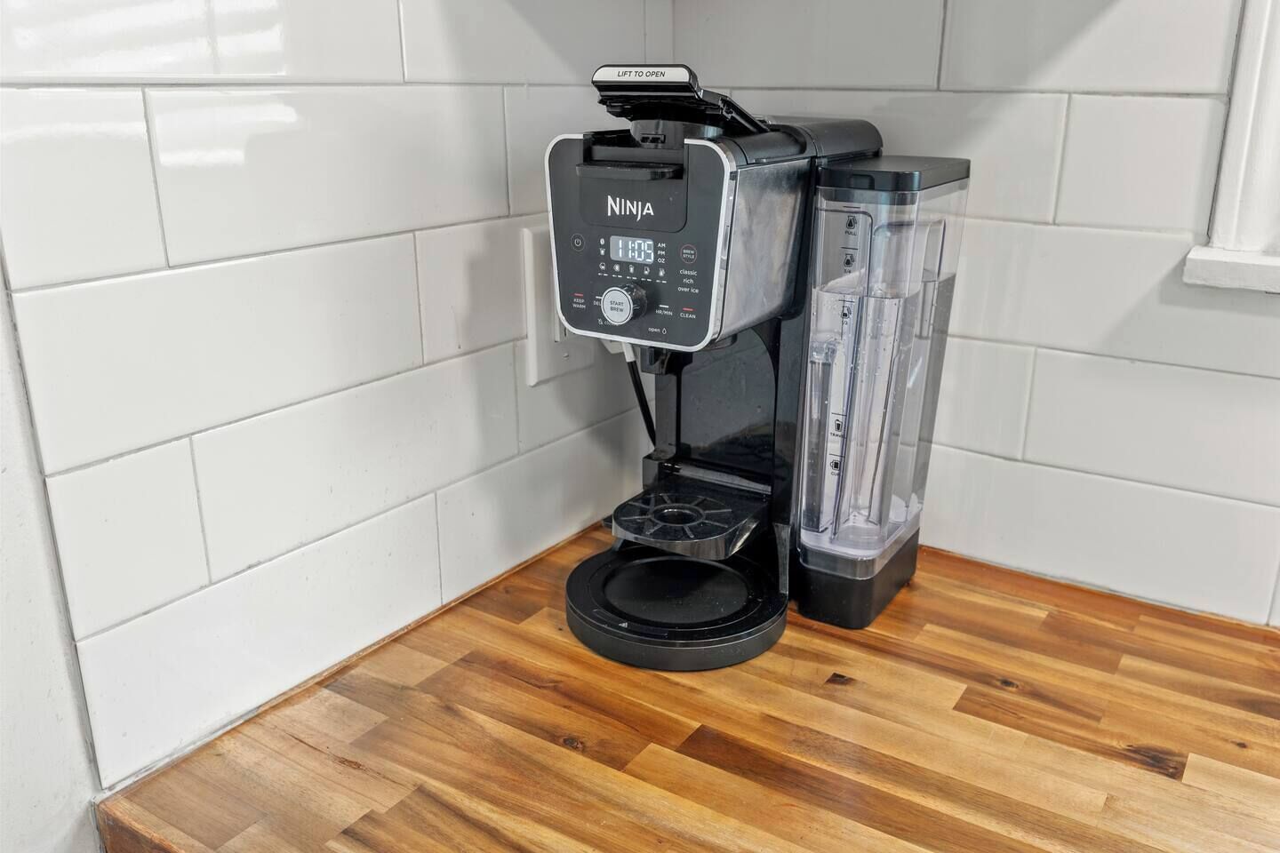 Une machine à café NINJA dotée d’un réservoir d’eau transparent et d’un bac d’égouttage noir, posée sur un comptoir en bois.