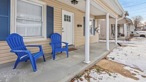 Ein eingeschossiges Haus mit überdachter Veranda, einer Haustür und zwei blauen Adirondack-Stühlen.