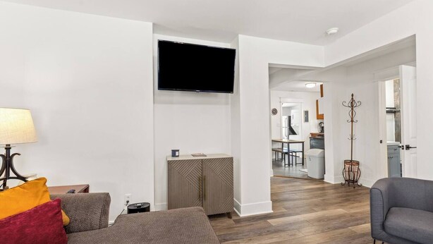 Ein modernes Wohnzimmer mit einer Couch, einem Fernseher und einer Lampe. Im Hintergrund ist eine Küche zu sehen.