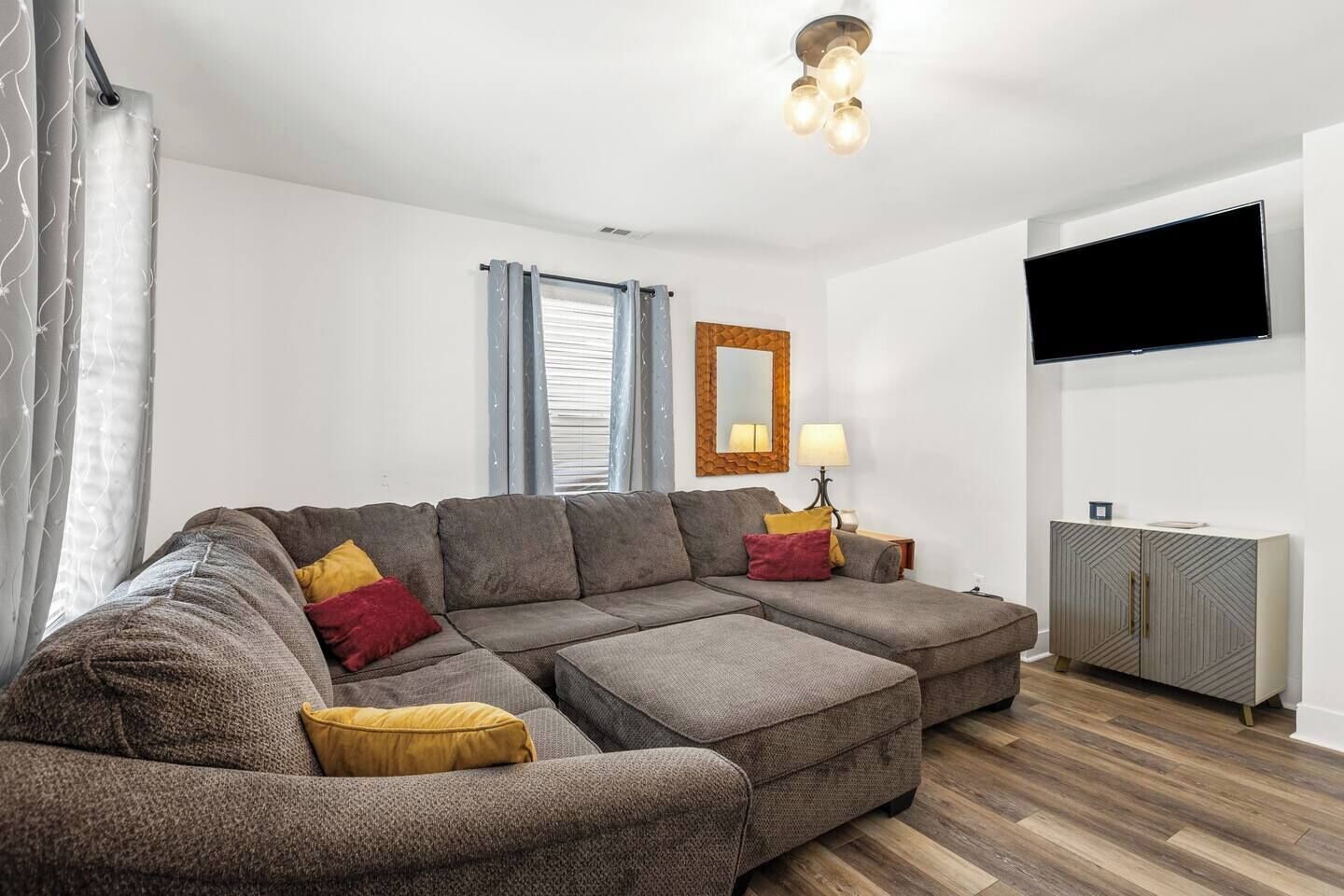 Een moderne woonkamer met een hoekbank, een aan de muur bevestigde televisie en een houten kast.