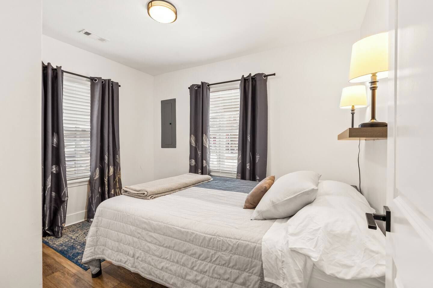 Een hotelkamer met een tweepersoonsbed, een nachtkastje met een lamp en een raam met gordijnen.