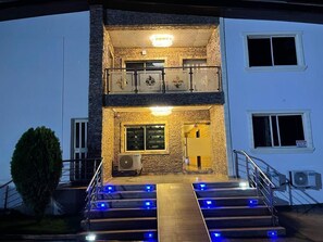 Un edificio de dos plantas con un balcón, una escalera con luces azules y un equipo de aire acondicionado.