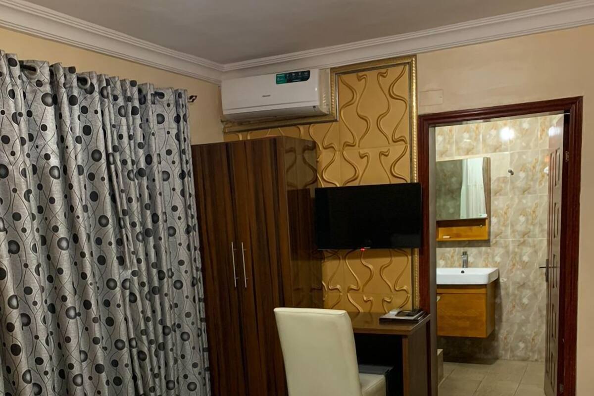 Une chambre d’hôtel comprenant un lit, un bureau, une chaise, une télévision et une salle de bain avec un miroir et un lavabo.