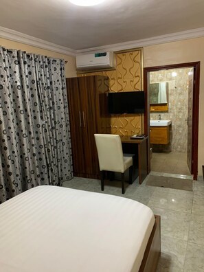 Habitación de hotel con cama, escritorio, silla, televisión y baño con espejo y lavamanos.